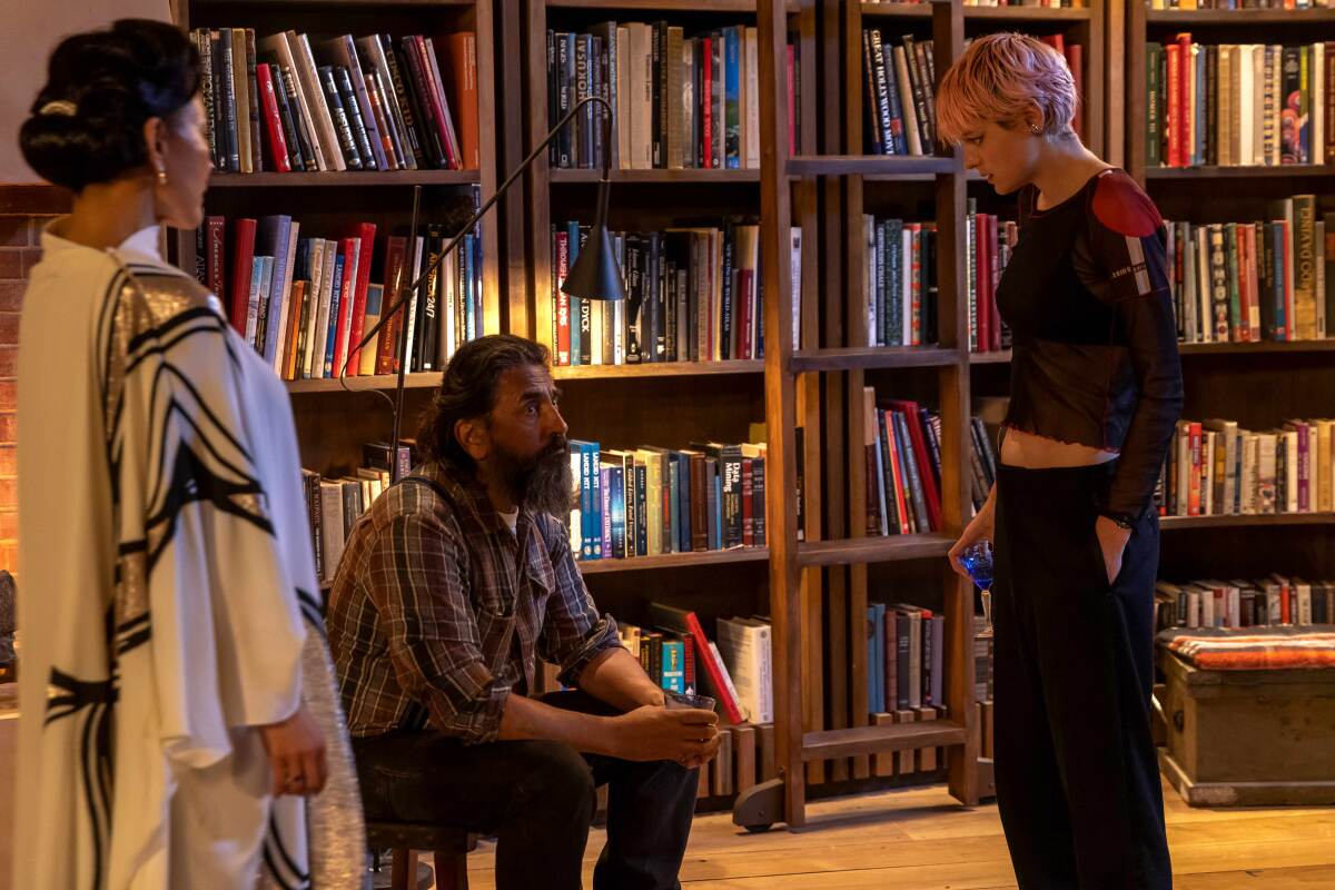 A man with a beard is flanked by two women in a library.