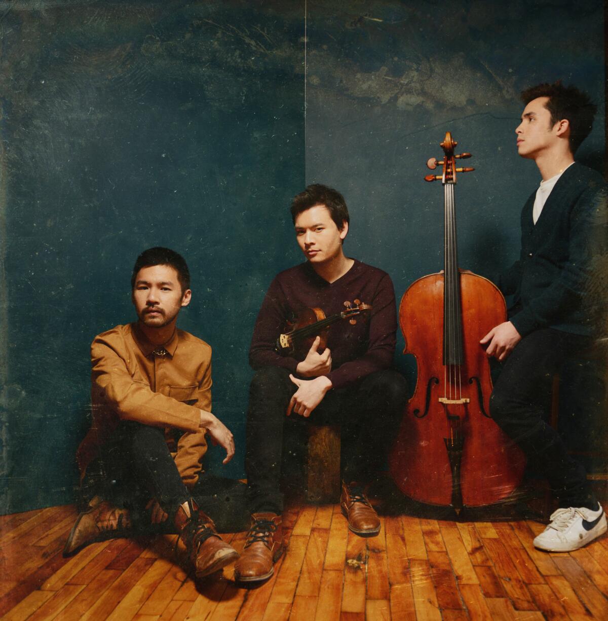 Three classical musicians sit in a corner with their instruments.