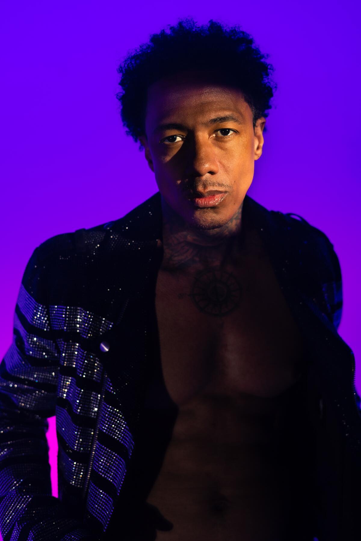 Nick Cannon poses for a portrait in a sparkly suit amid purple lighting