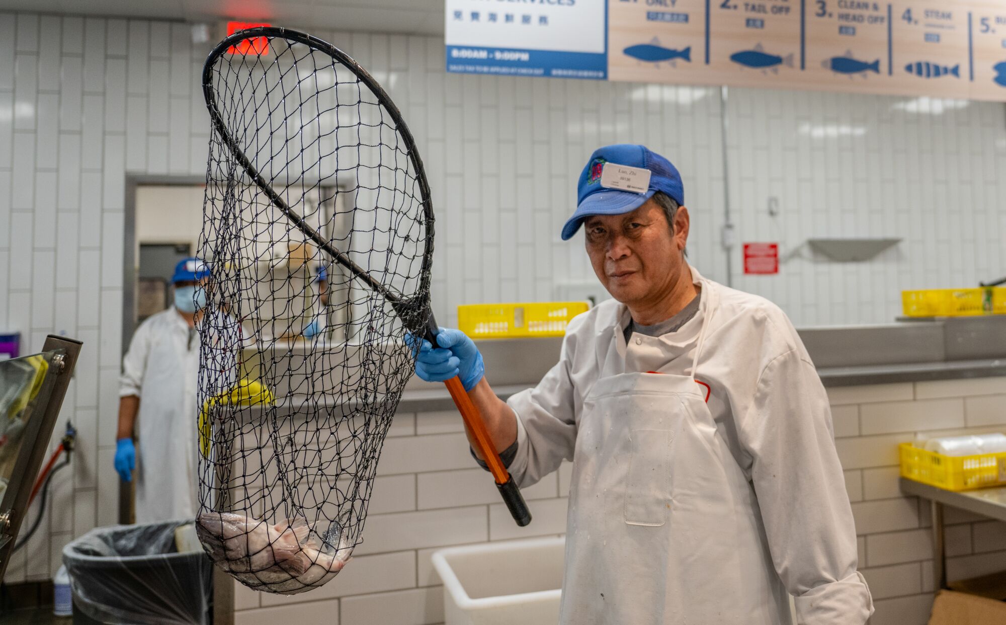 Un préposé au comptoir du poisson tient un sébaste vivant dans un filet. 