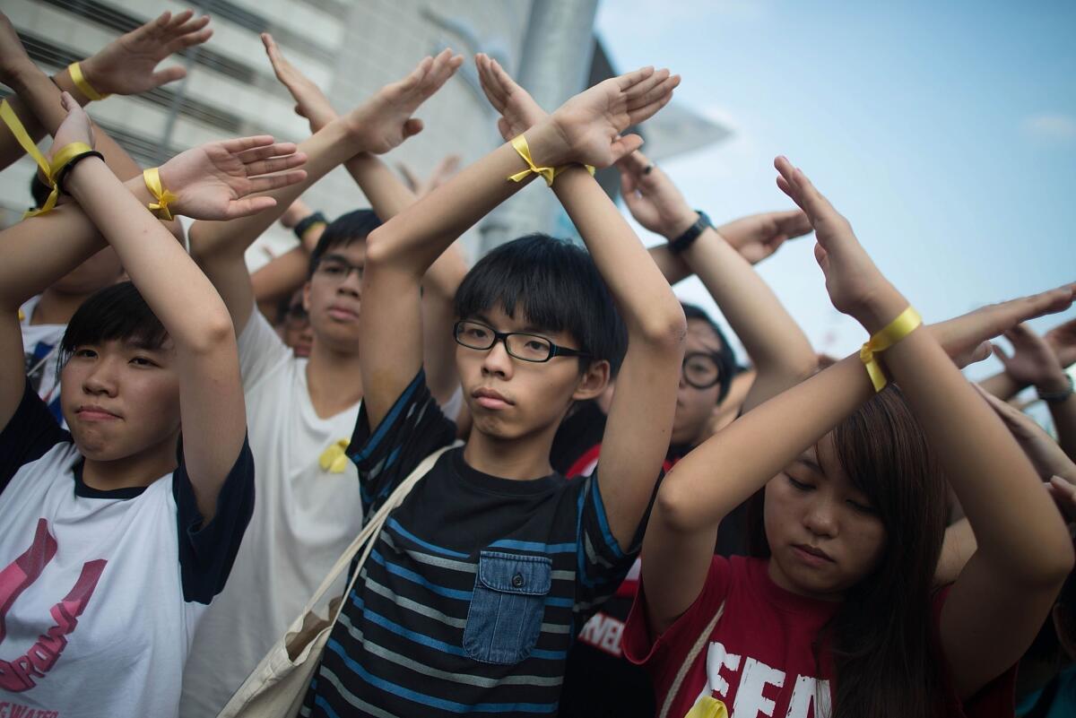 Joshua Wong, center, and other protesters turn their backs and raise crossed hands in silence at a flag-raising ceremony at Golden Bauhinia Square in Hong Kong.