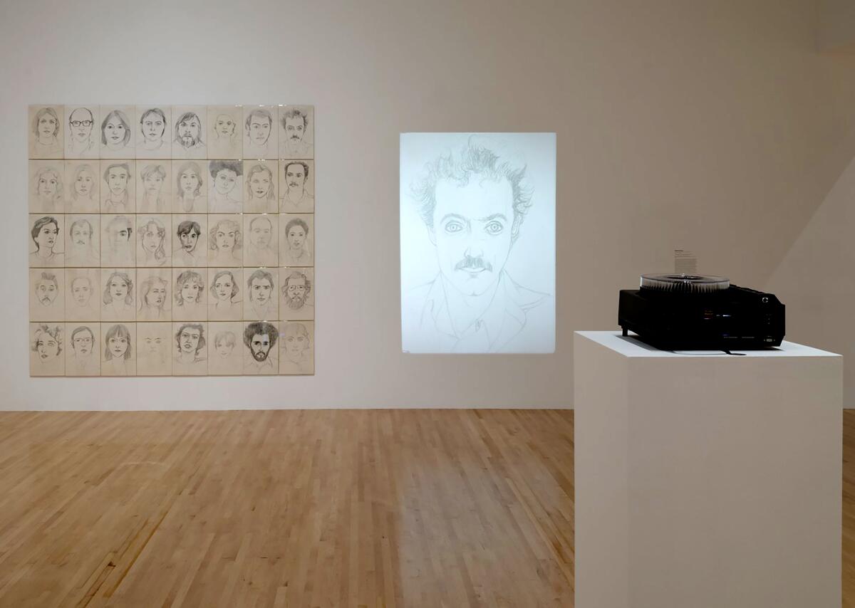 In a museum gallery, a portrait of a man is projected on a wall next to a grid of smaller portraits
