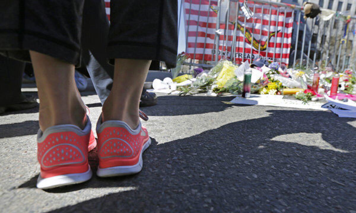 A woman in running shoes pauses at a makeshift memorial on Boylston Street near the finish line of Monday's Boston Marathon explosions.