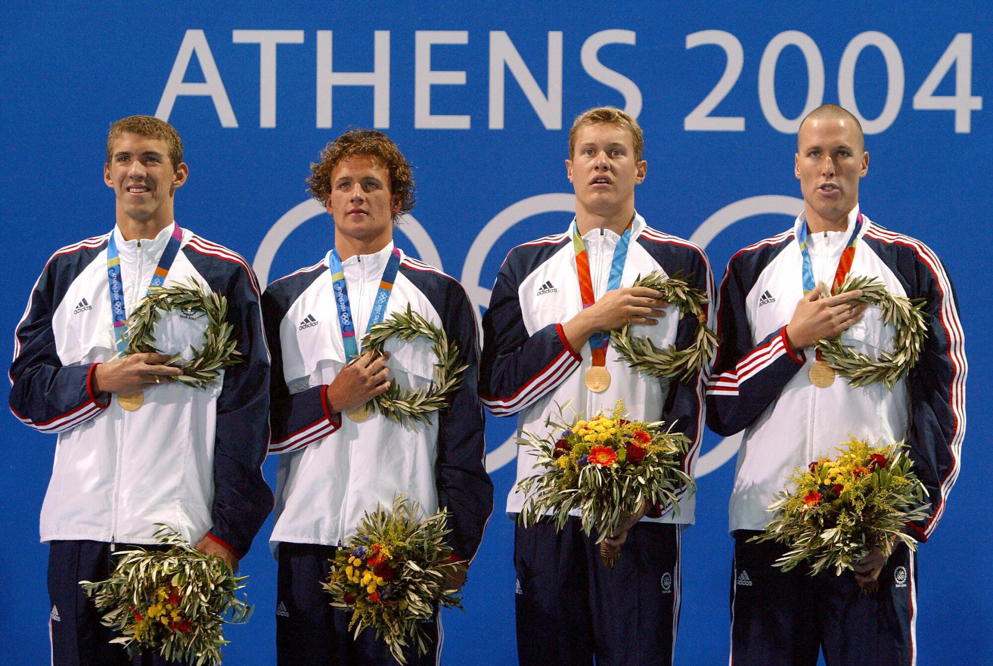Members of the U.S. men's relay team on a victory podium before a sign that says "Athens 2004"