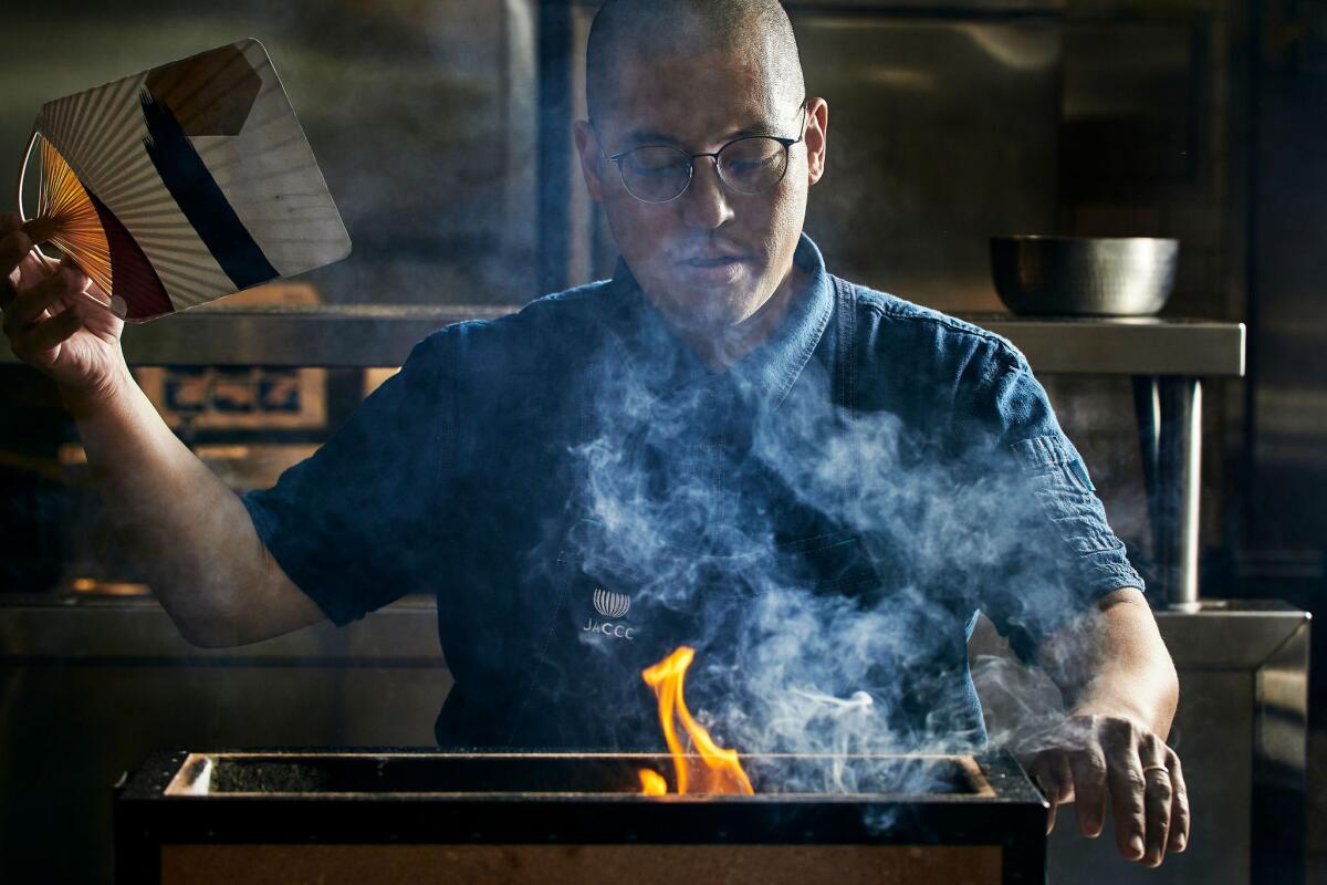 A photo of chef Chris Ono fanning the flames of a small Japanese charcoal grill for his new dinner series, Hansei.