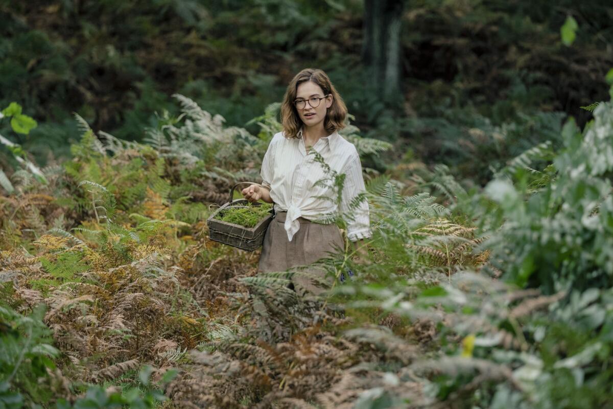 Lily James carries a basket of plant cuttings in the movie "The Dig."