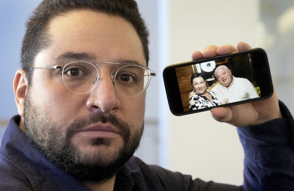 Yan Skvyeskyi poses with a smarthphone showing his parents Irina and Igor Kushnir prior to an interview with the Associated Press in Berlin, Germany, Tuesday, March 1, 2022. Ukrainian Skvyeskyi, who works in sales in Berlin, immigrated to Germany in 1990, after the collapse of the Soviet Union. As Russia's war in Ukraine drags into its second week, more than 1.5 million Ukrainians immigrants living in other European countries, are watching on in agony, horror and fear as their relatives and friends back home are looking for shelter in bunkers or are desperately trying to flee the country. (AP Photo/Michael Sohn)
