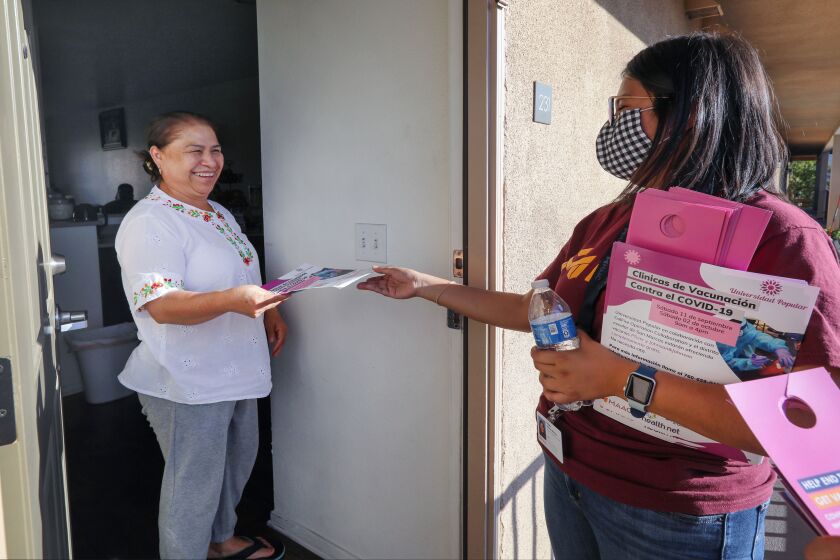 October 1, 2021, San Marcos, California_USA_| On a late Friday afternoon in the Richmar neighborhood resident Catalina Valentine, left, receives a flyer from Maac Head Start program volunteer Nathalie Martinez who came to her apartment door with information about the next day's Covid-19 vaccination clinic to be held at nearby San Marcos Elementary School. |_ Photo Credit: Photo by Charlie Neuman
