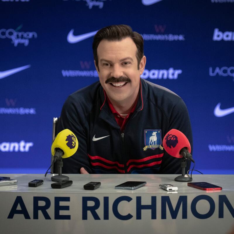 A smiling man sits at a podium for a news conference