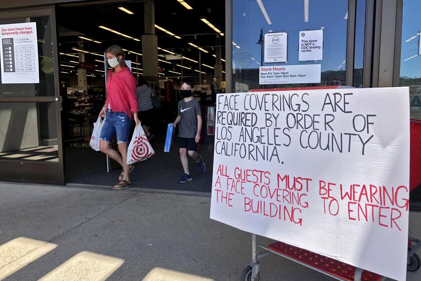 Shoppers come out of Target where a new hand-made sign reminds guests must wesr fasce covering while shopping, in La Canada Flintridge on Wednesday, April 15, 2020.