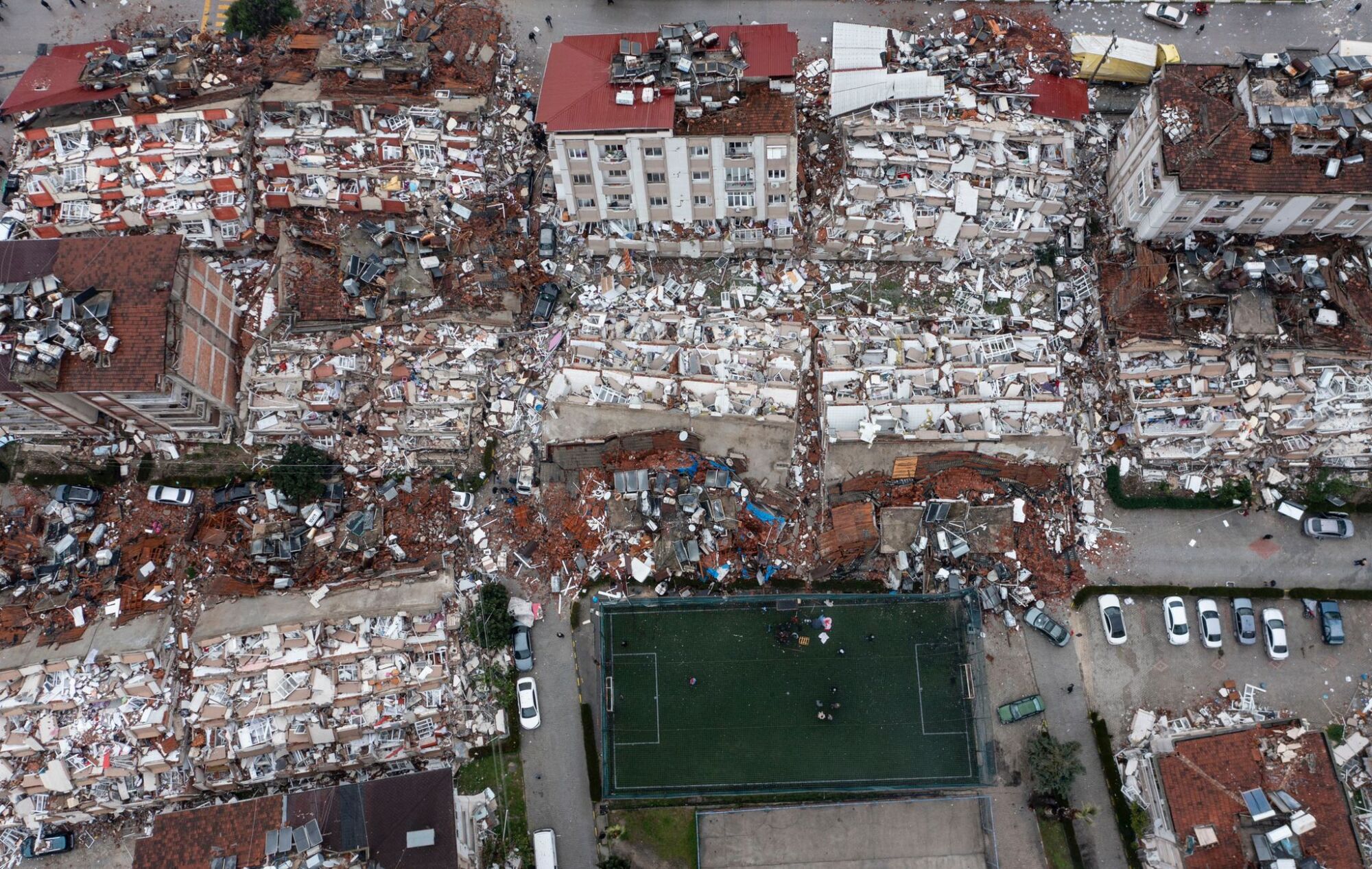 An aerial view of debris of a collapsed buildings near a clean soccer field.