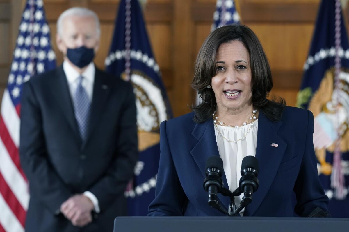 President Biden listens and stands in the background as Vice President Kamala Harris speaks at a podium