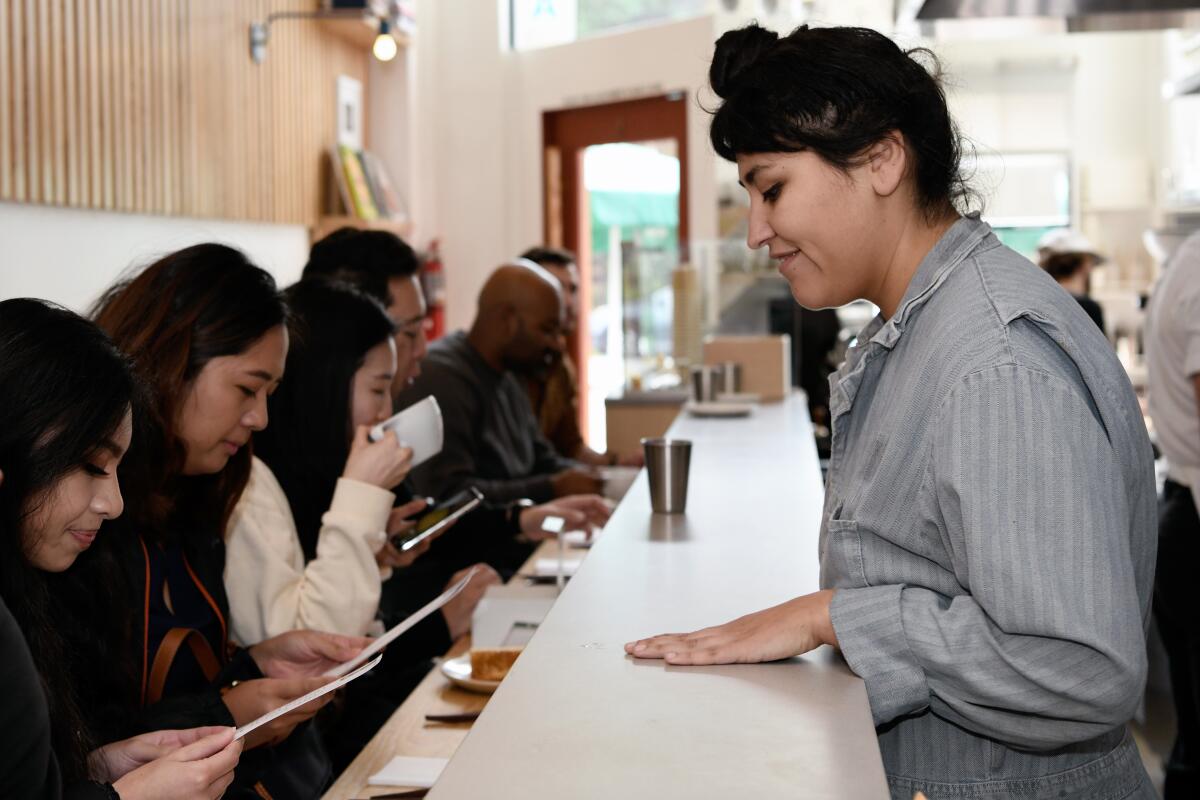 A woman in a loose collared shirt tends to customers seated at Konbi's intimate countertop in 2019.