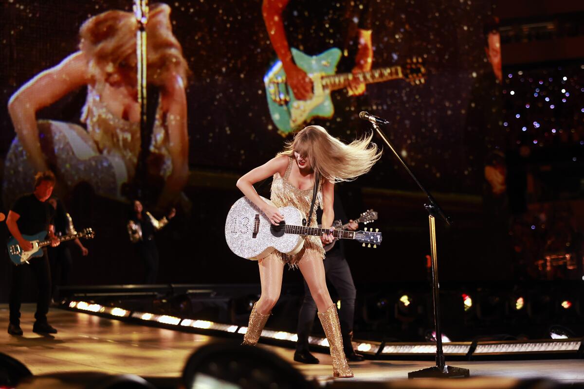 Taylor Swift plays a guitar while her hair flies on stage.