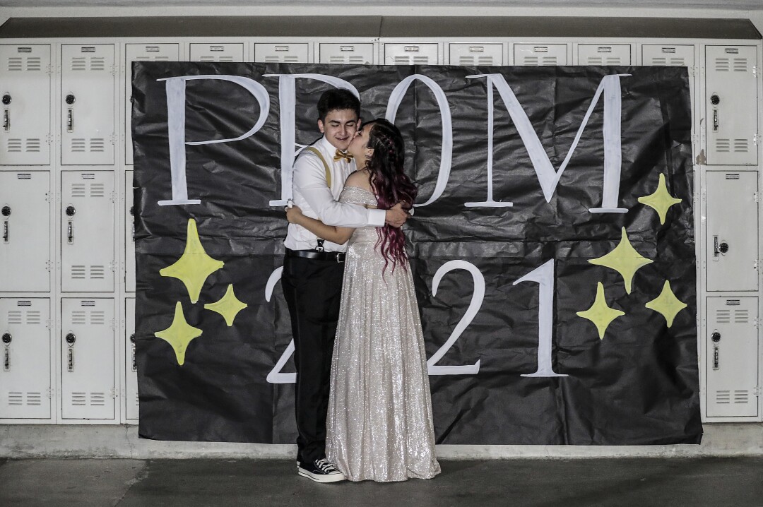 High school sweethearts embrace in front of lockers at their on-campus prom.