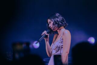 Singer-songwriter Gracie Abrams, in taupe sleeveless top with metal details, holds a microphone at her Sept. 8 show in L.A.