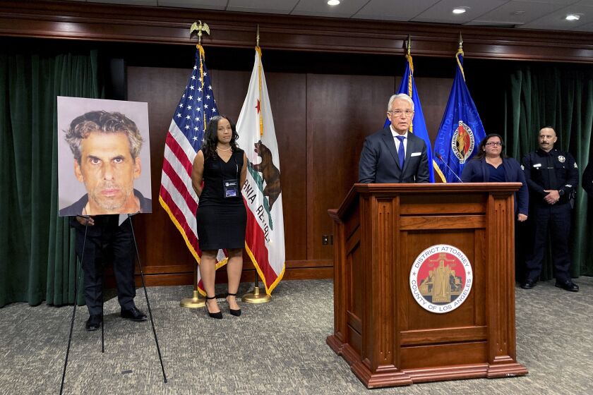 Los Angeles District Attorney George Gascon, at podium stands by a photo on display of TV producer Eric Weinberg during a news conference to announce sexual assault charges against Weinberg on Wednesday, Oct. 5, 2022 in Los Angeles. (AP Photo/Christopher Weber)