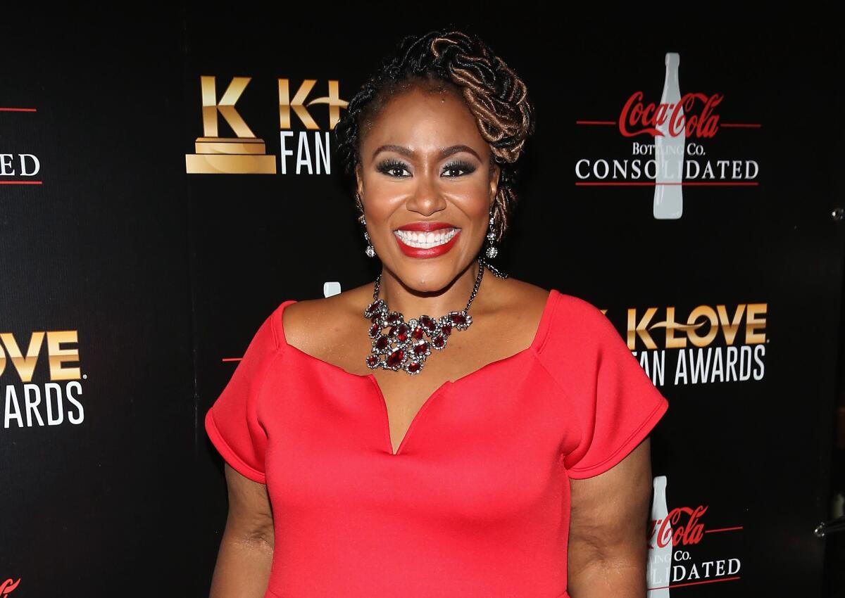 Mandisa smiling a huge smile and wearing a short-sleeved red dress and statement necklace