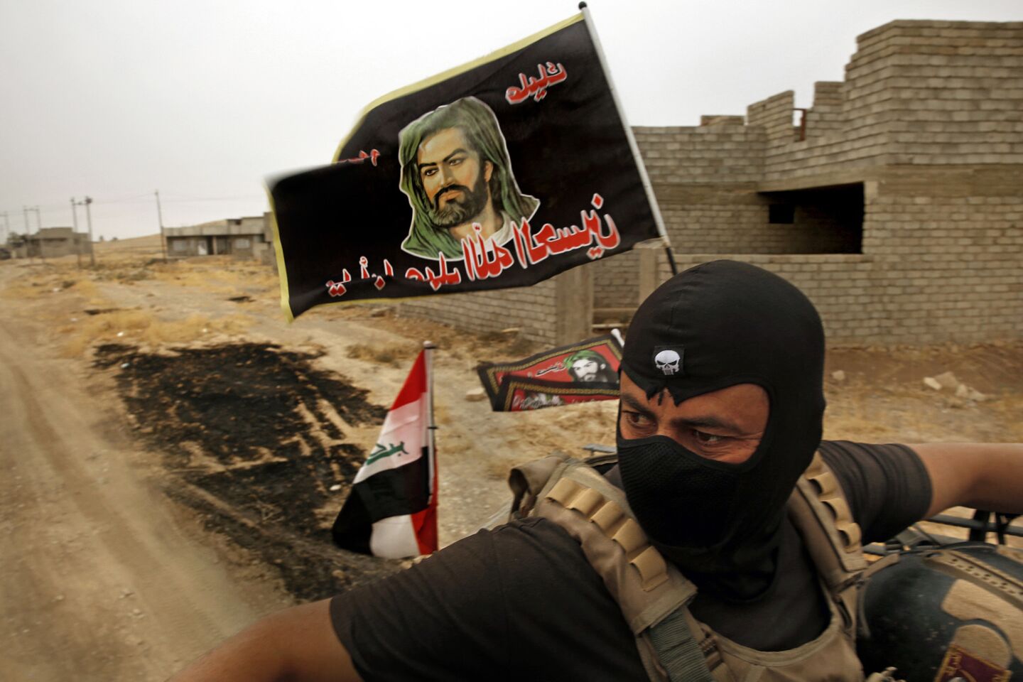 An Iraqi special forces member rides in the turret of a humvee with a Shiite religious banner flying behind him as he patrols Bartella, Iraq.
