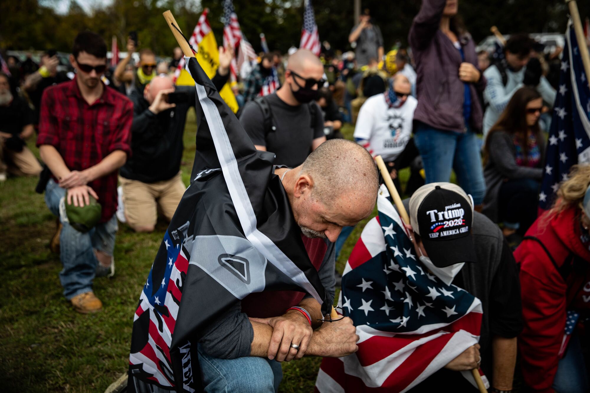 People with U.S. flags and Trump 2020 hats kneel in a park