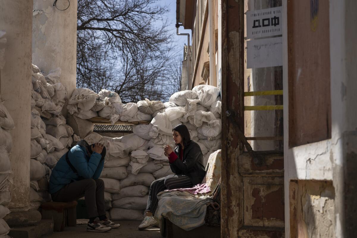 Two people sit next to a stack of sandbags.