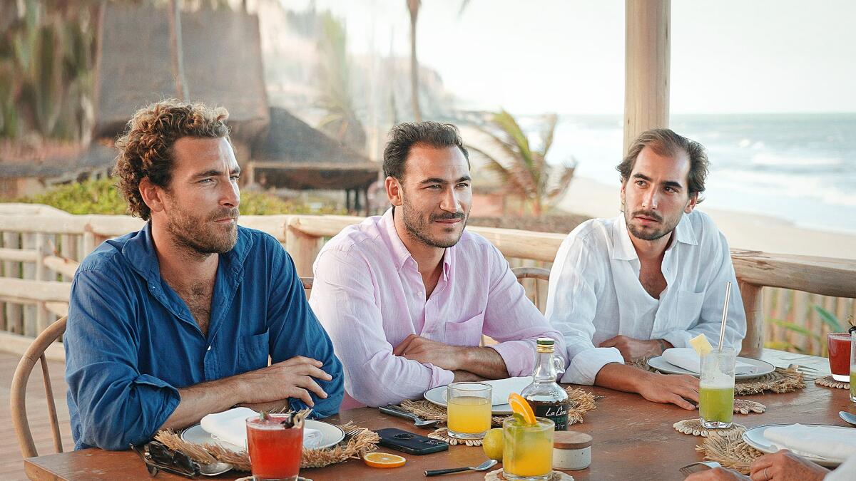 Three men in button-down shirts sitting at a table by the beach