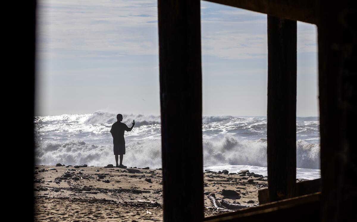The silhouette of a man standing on a beach in front of waves.
