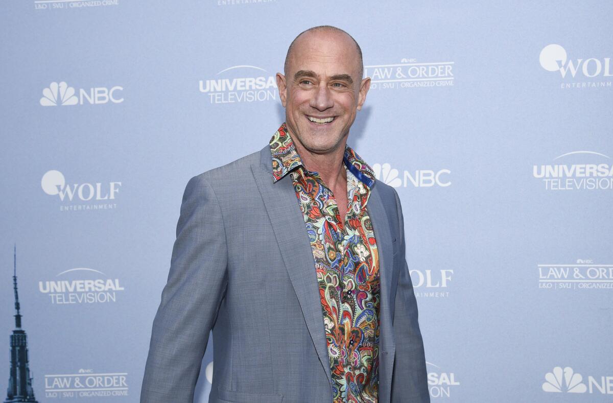 A man with a shaved head wears a gray suit jacket, a colorful shirt and a smile for photographers.