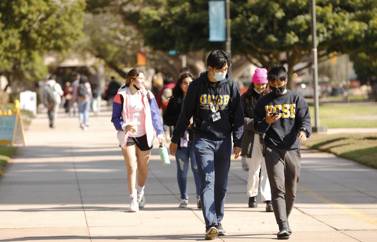 Masked students walk outside on a college campus.