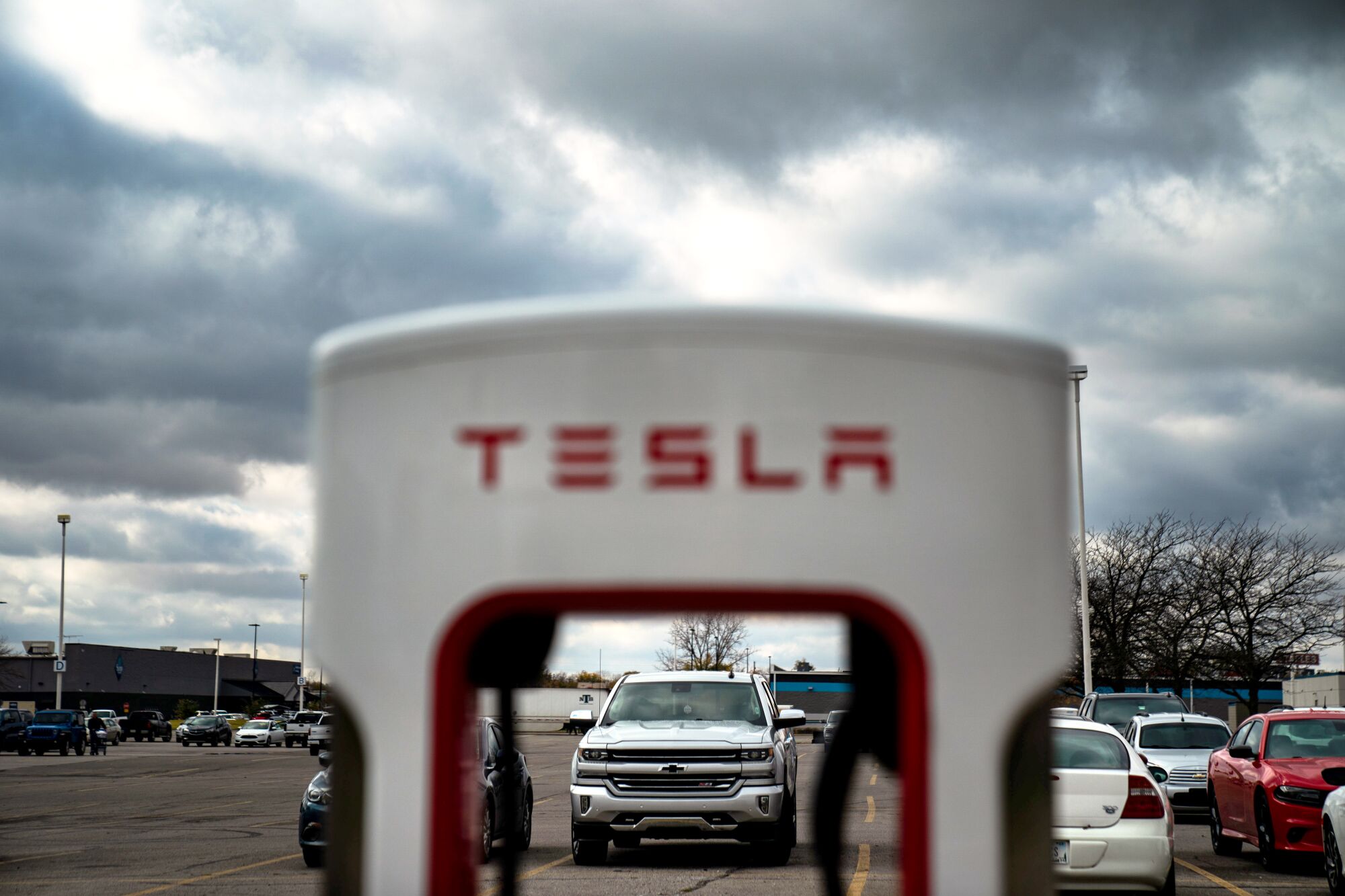 A white structure with the word Tesla, in red, with cars in the background against cloudy skies