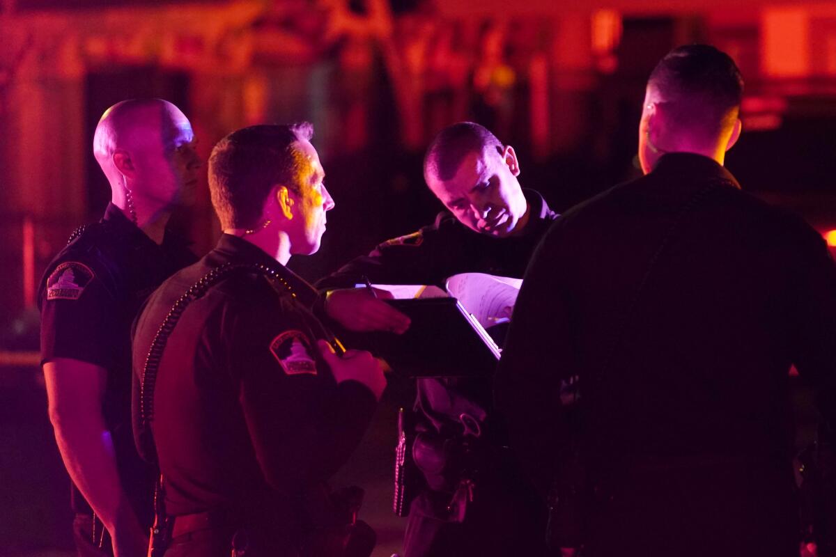 A group of men in law enforcement uniforms look at paperwork in the light of police car lights.