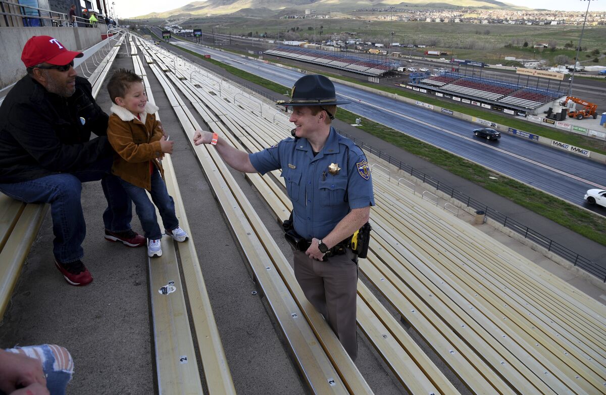 Colorado State Patrol Trooper Josh Lewis fist bumps 3-year-old Lincoln Delagarza, of Northglenn, Colorado, before racing begins at Bandimere Speedway west of Denver on May 5, 2021. The State Patrol runs a program called "Take it to the Track" in hopes of luring racers away from public areas to a safer and more controlled environment, even allowing participants to race a trooper driving a patrol car. The program's goals have gained new importance and urgency this year as illegal street racing has increased amid the coronavirus pandemic. (AP Photo/Thomas Peipert)