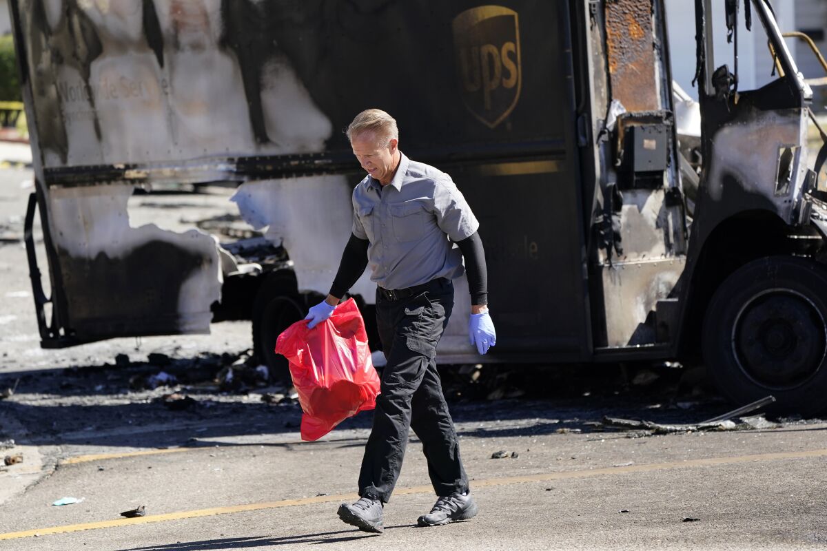 An official from the San Diego County medical examiners office carries items from the site of a plane crash Tuesday, Oct. 12, 2021, in Santee, Calif. Recordings indicate the pilot of a twin-engine plane nose-dived into this San Diego suburb Monday despite a growingly concerned air traffic controller who repeatedly warned the pilot to climb in altitude — information that will be examined by investigators who arrived at the crash scene on Tuesday. (AP Photo/Gregory Bull)