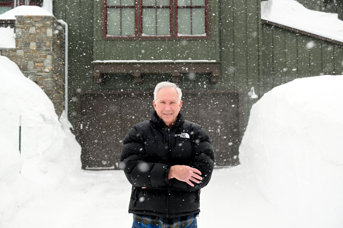 A man in a black coat stands outside in the snow.