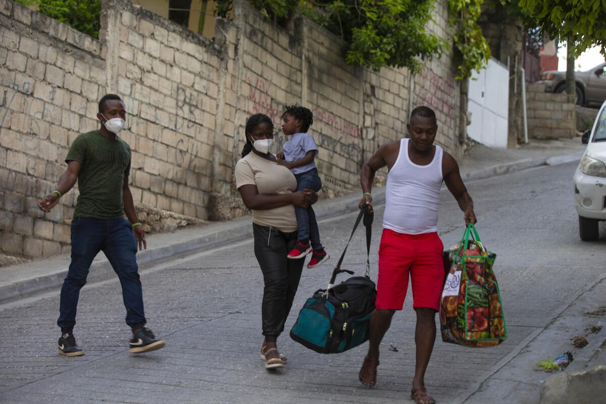 Two men, one carrying luggage, and a woman carrying a child on a street