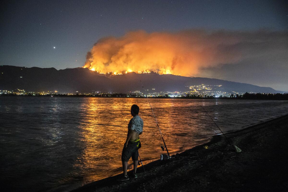 Felipe Montiel fishes at Lake Elsinore as the Holy fire reflects across the water while burning in the Cleveland National Forest.