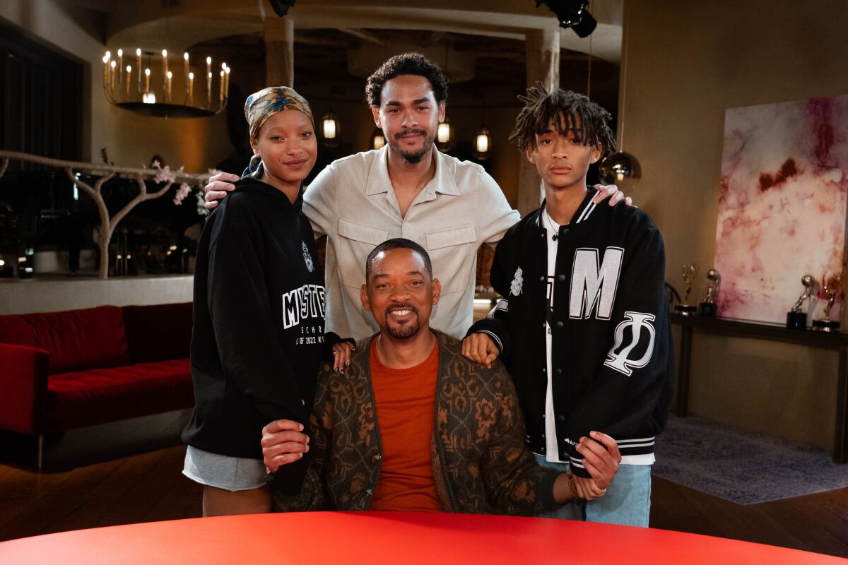 A man seated at a red table with three young people standing behind him