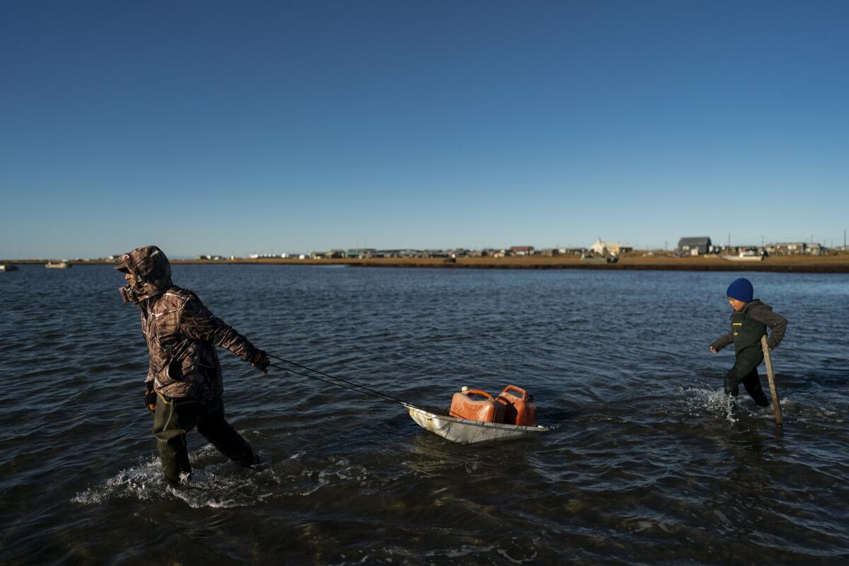 Man pulls a sled with fuel containers in a lagoon. A small boy walks behind