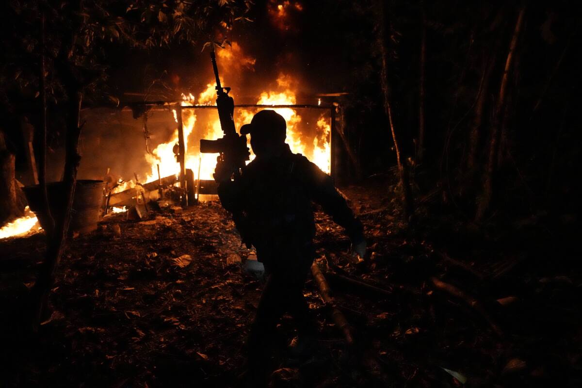 An armed man is silhouetted against flames.