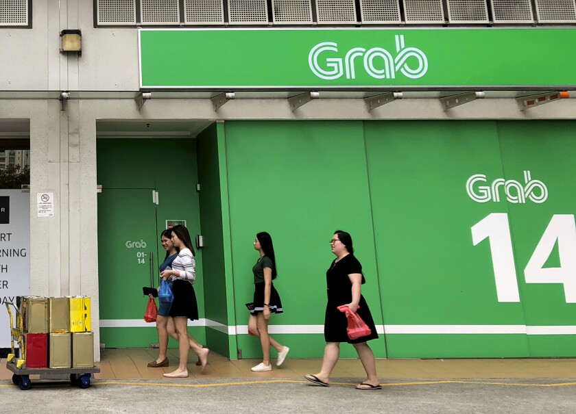 FILE - Office workers walk past Grab offices during their lunch hour in Singapore on March 26, 2018. Southeast Asia’s largest ride-hailing company Grab made its market debut Thursday, Dec. 2, 2021, following a $40 billion merger in a special purpose acquisition company deal. (AP Photo/Wong Maye-E, File)