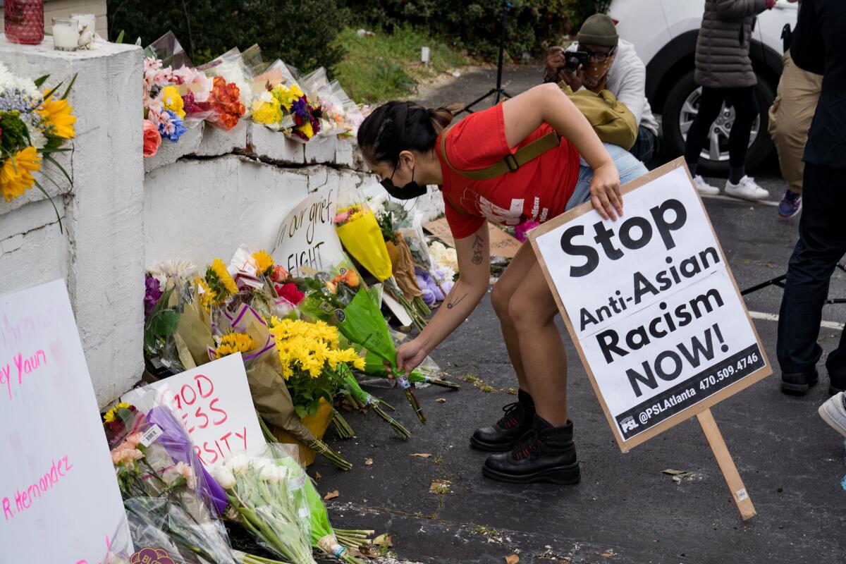A person holding a "Stop Anti-Asian Racism Now!" sign leaves flowers at a memorial