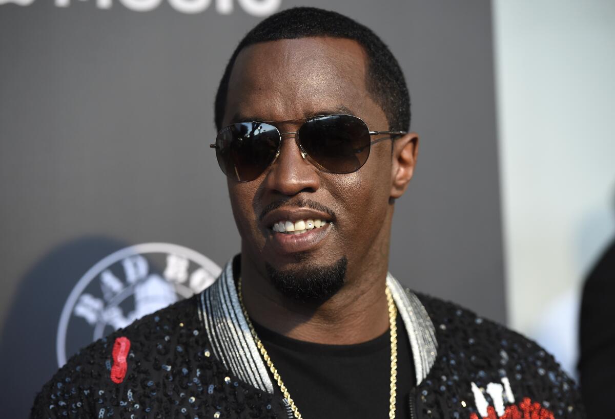 Diddy smiles while wearing black aviator glasses and a sparkling bomber jacket