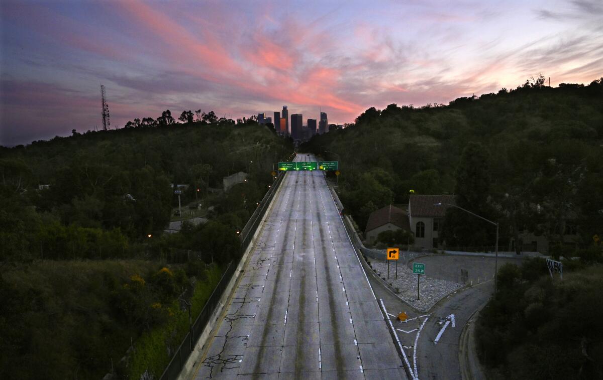 An empty freeway with the downtown L.A. skyline in the background at sunset
