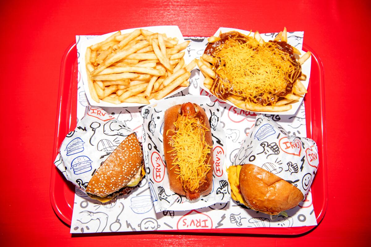 An overhead photo of burgers, chili dogs and fries atop a red plastic tray.