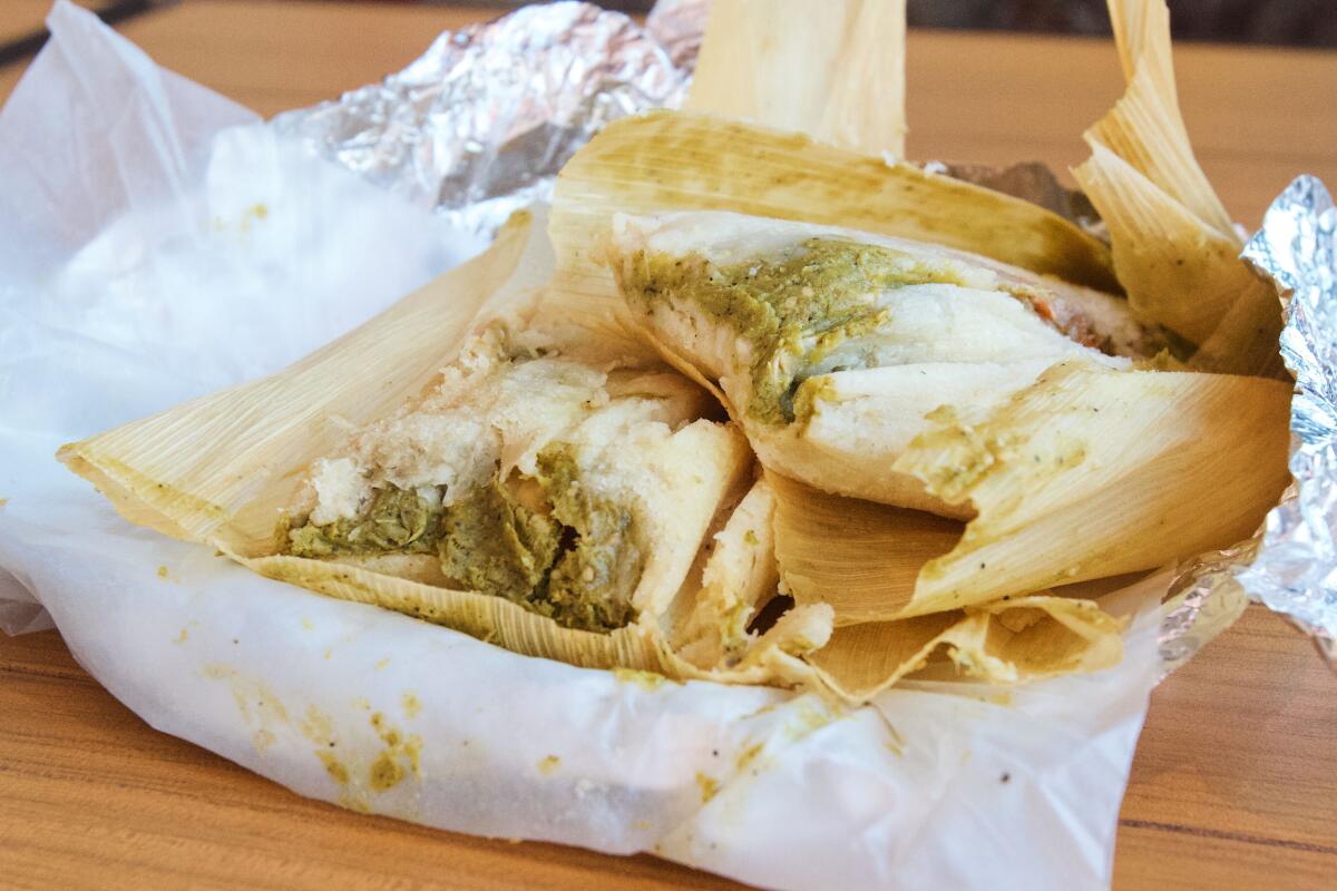 Two verde tamales partially in their husks stacked atop each other at Guisados.