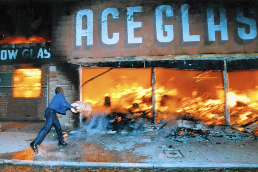 A shop owner hurls a bucket of water on a fire raging at a business next to his during the 1992 Los Angeles riots. 