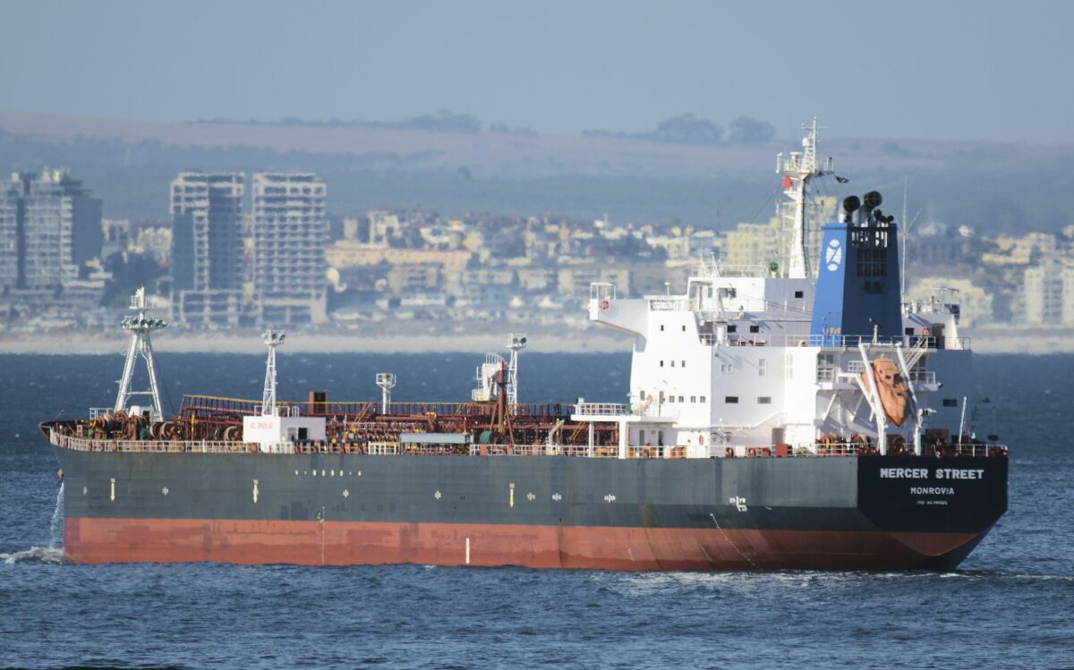An oil tanker on the water with a seaside city in the background.