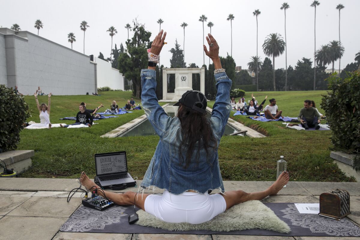 A woman with a laptop in front of her leads an outdoor yoga class 