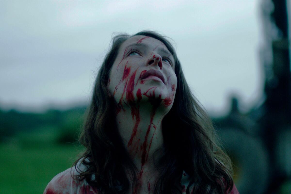 A woman with blood on her face looks up to the sky.
