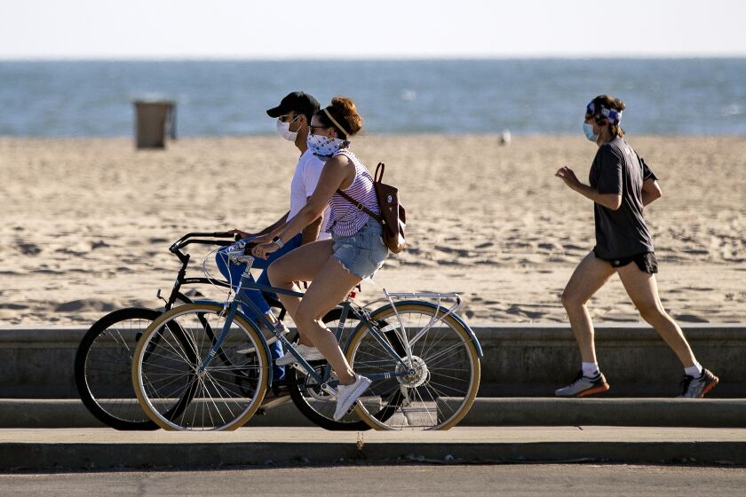 SANTA MONICA, CA - JULY 3, 2020: Bicyclists and a runner wear masks as they enjoy the boardwalk at Santa Monica Beach on Friday as all beaches in L.A. County are closed due to the coronavirus pandemic on July 3, 2020 in Santa Monica, California. (Gina Ferazzi / Los Angeles Times)